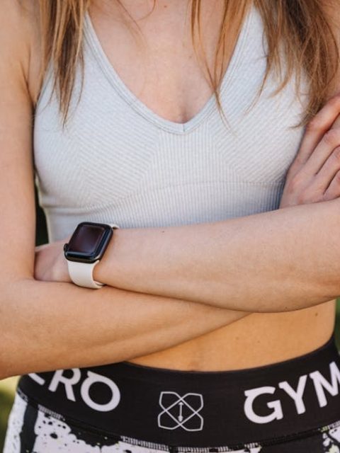Confident woman in a sports bra and leggings, arms crossed, outdoors.