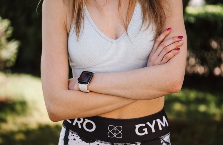 Confident woman in a sports bra and leggings, arms crossed, outdoors.